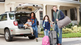 Family with two children (3 and 9 years) going on vacation, loading luggage into car.  Main focus on girl and father.