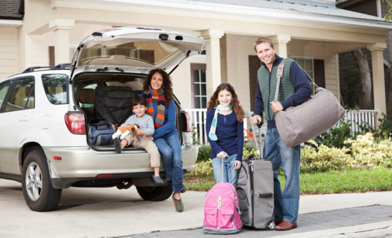 Family with two children (3 and 9 years) going on vacation, loading luggage into car.  Main focus on girl and father.