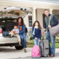 Family with two children (3 and 9 years) going on vacation, loading luggage into car.  Main focus on girl and father.